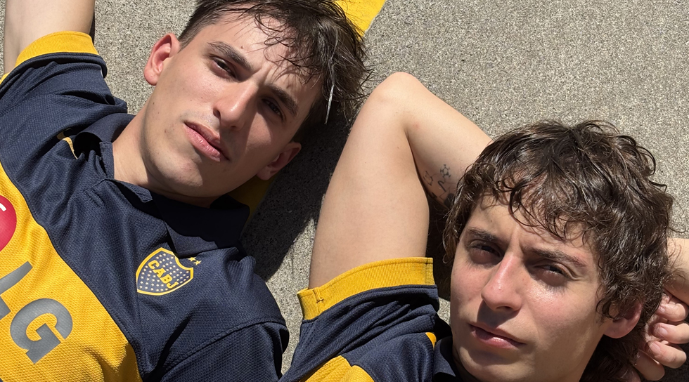 Dos actores con camisetas de boca recostados al sol